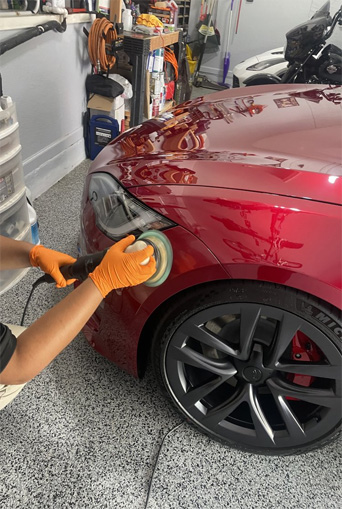 Professional car detailing service by Broward Detailers featuring a technician polishing a red vehicle in a clean garage setting.