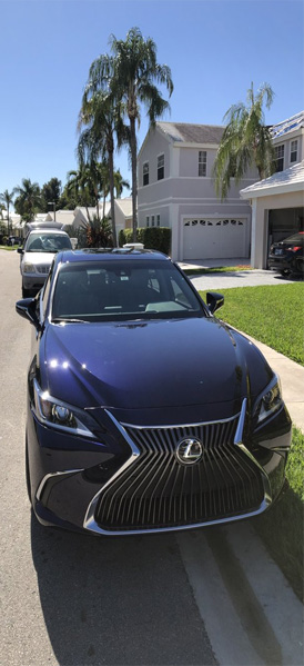 Sleek blue Lexus parked in a residential area with palm trees and a modern home in the background, representing the quality car detailing services by Broward Detailers in South Florida.