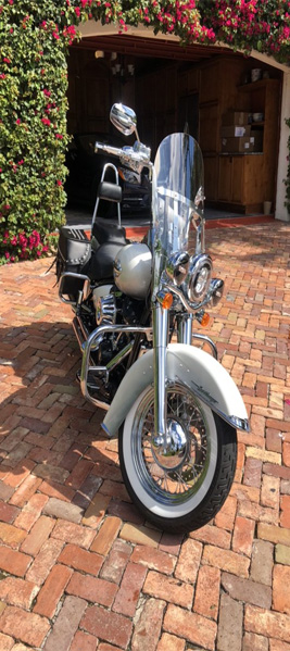 Classic chrome motorcycle with a stylish windshield parked on a brick driveway, surrounded by vibrant flowers, representing the premium detailing services offered by Broward Detailers in South Florida.