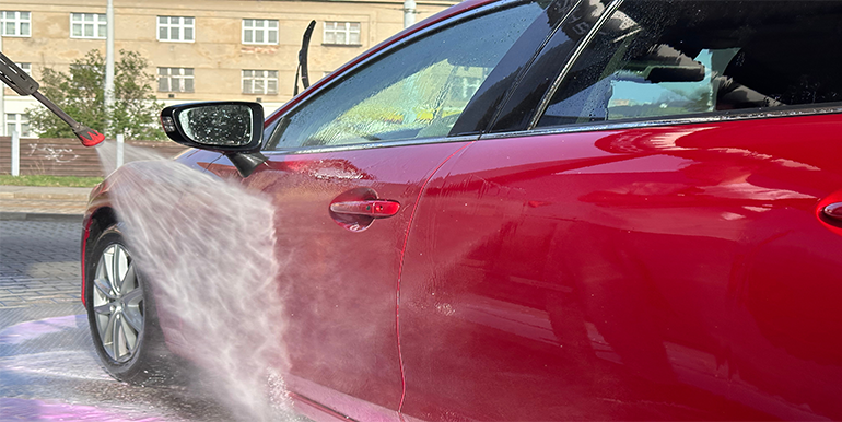 Professional mobile car wash service in South Florida, featuring a high-pressure water spray on a shiny red vehicle for a spotless clean.