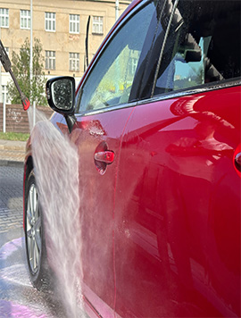 High-pressure mobile car wash service in South Florida, showcasing a technician washing a red vehicle with a water spray for a pristine finish.